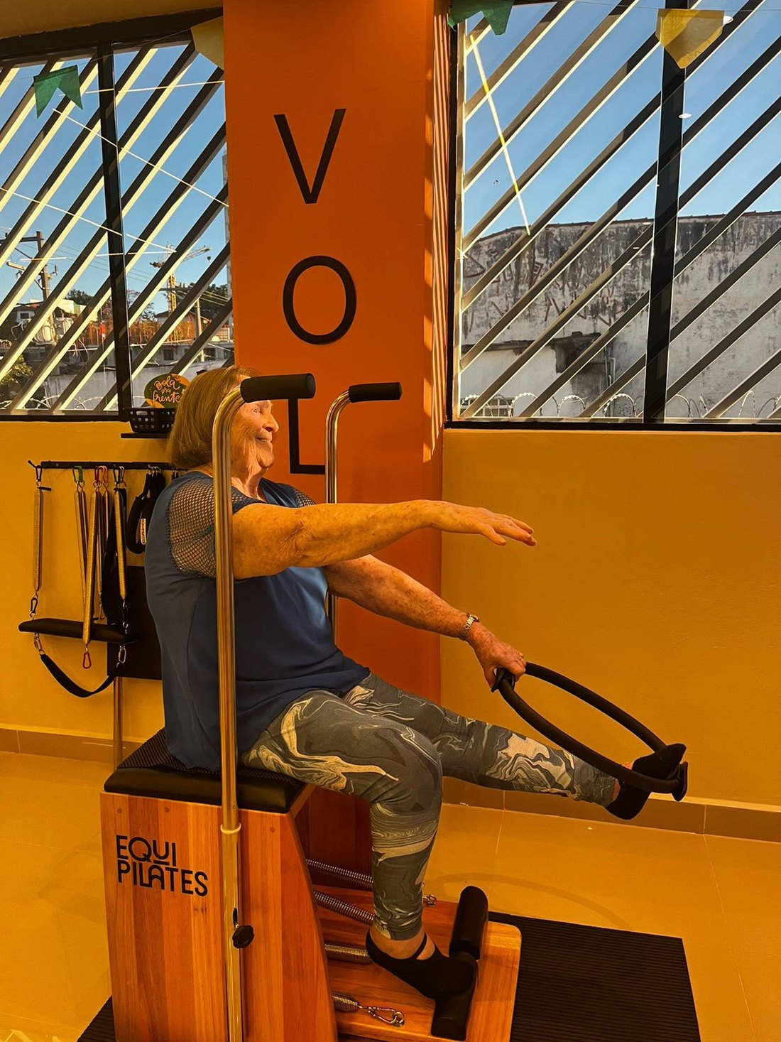 Aluna na Chair de pilates trabalhando braços e postura com acompanhamento da instrutora